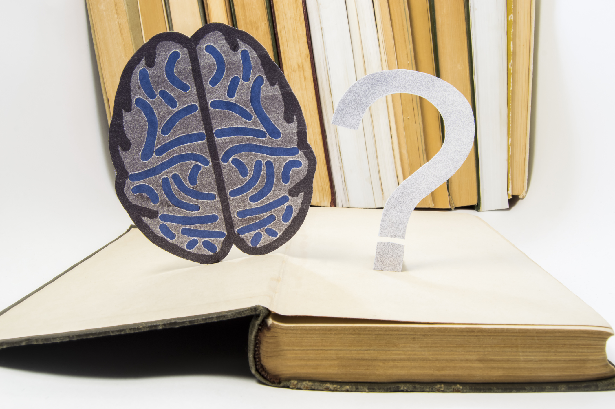 Paper brain silhouette and question mark is over old open medical book. Photo to refer issues and questions in study of brain, as well as difficulties in diagnosis in neurology and neuroscience