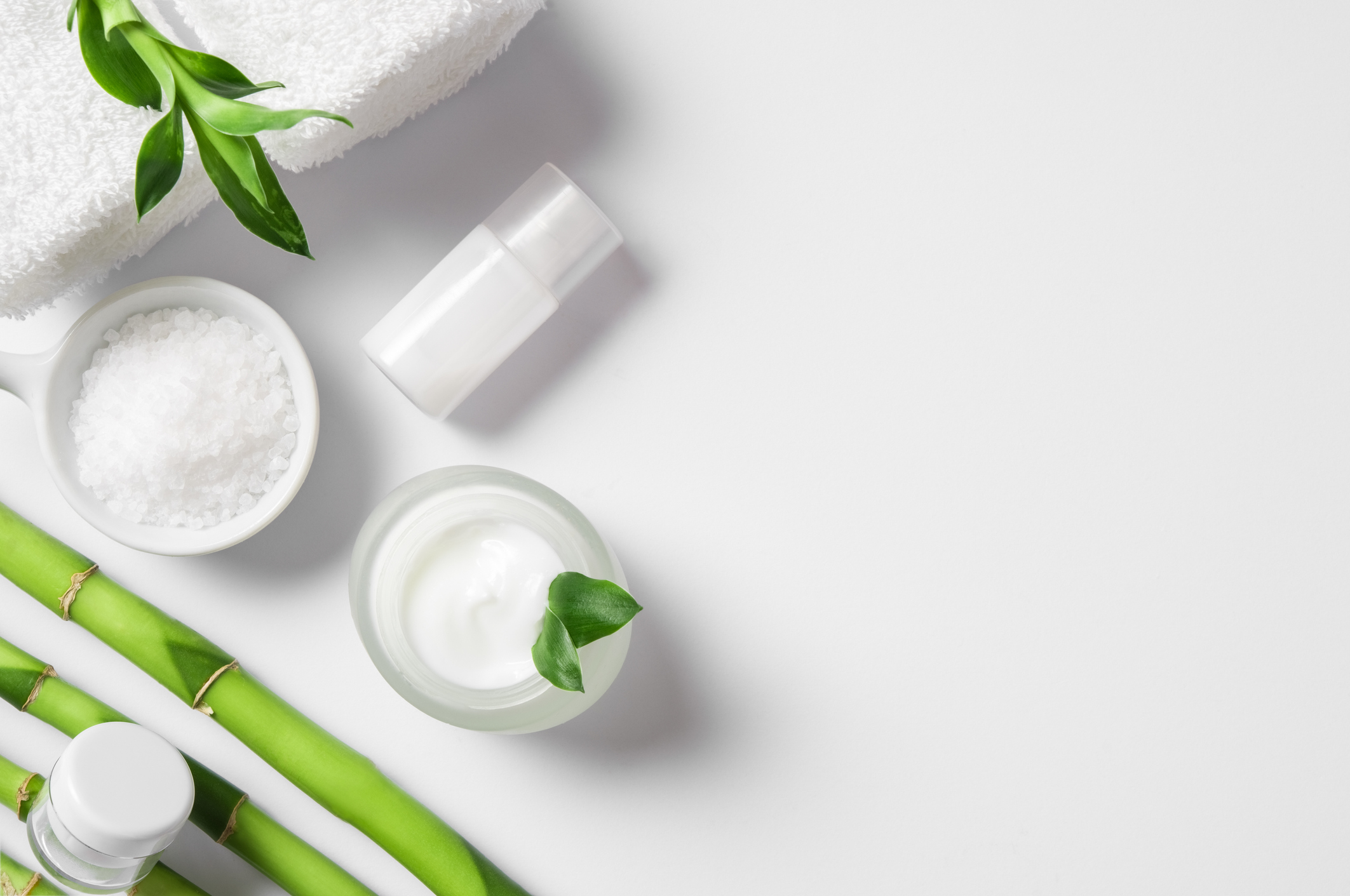 Top view of cosmetic products with natural ingredients on white background for natural beauty. High angle view of spa setting with natural moisturizer and bamboo sticks. Beauty spa background with copy space.