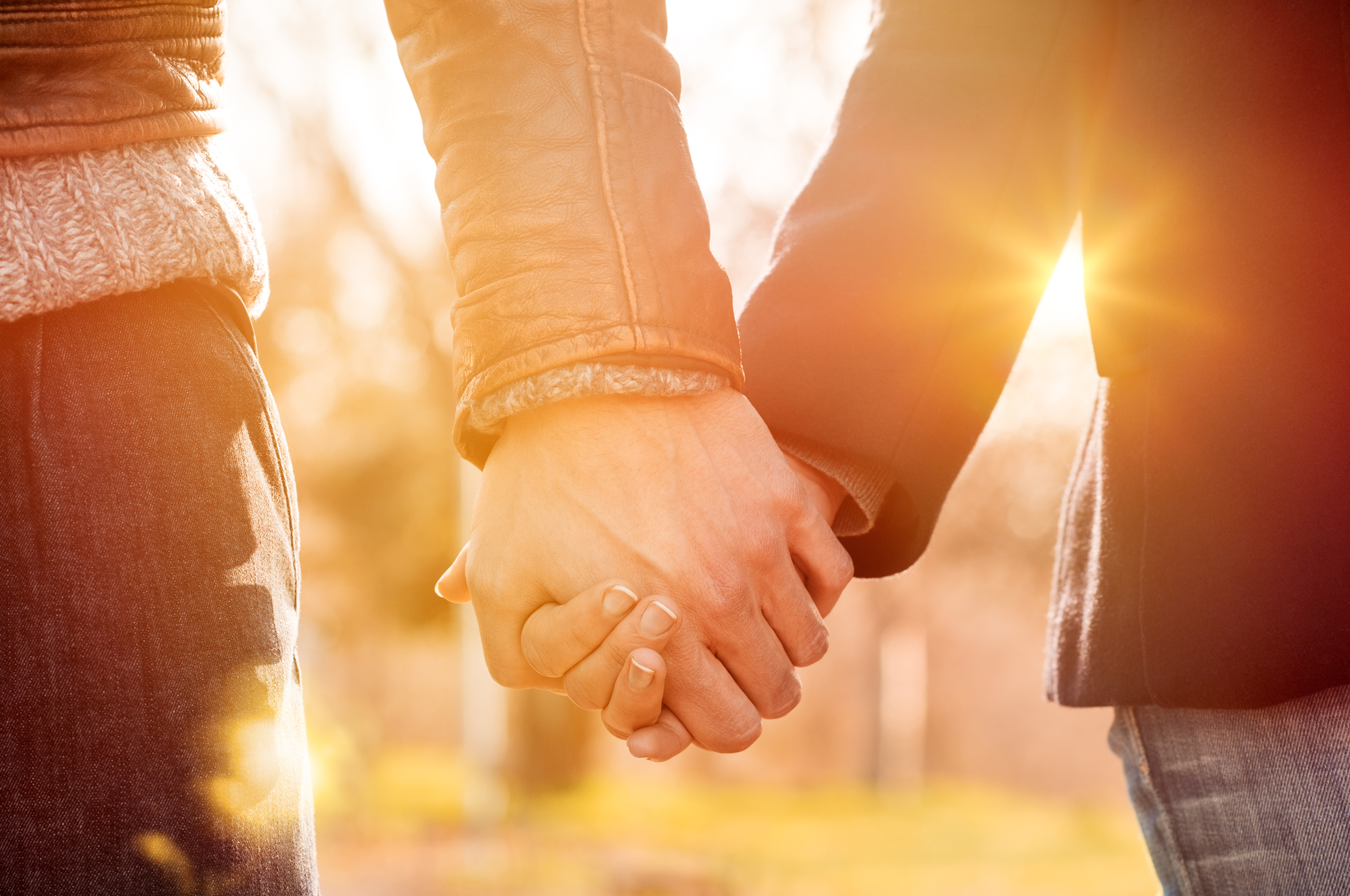 Closeup of loving couple holding hands while walking at sunset.