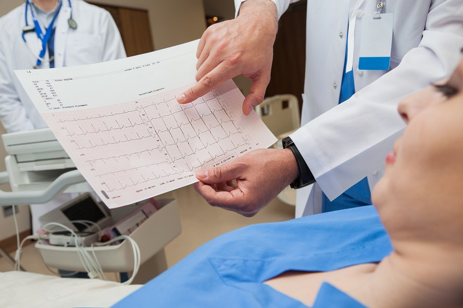 Close-up of a doctor, hands only, showing a normal sinus rhythm sheet to a young female patient.