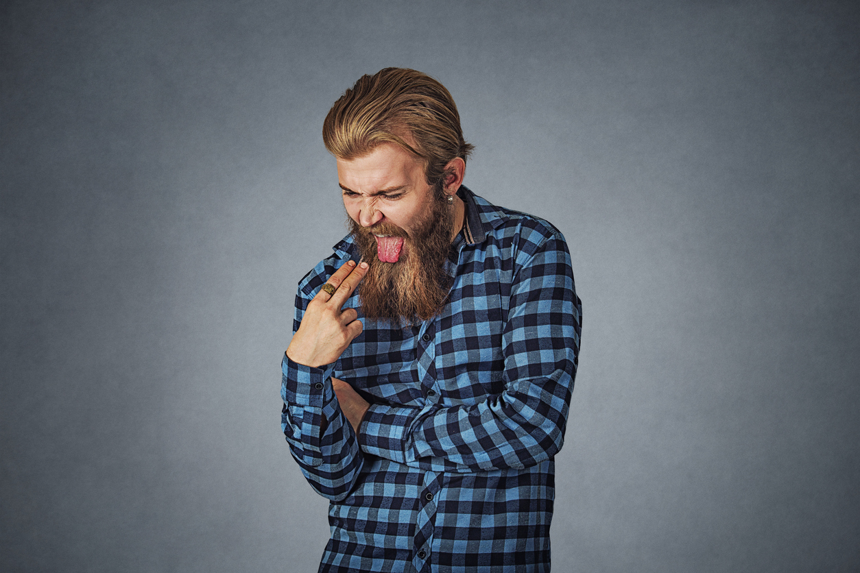 Disgusted man with finger in mouth displeased wants to throw up. Hipster male with beard in blue plaid checkered shirt  Isolated on gray grey studio Background. Negative face expression, human emotion