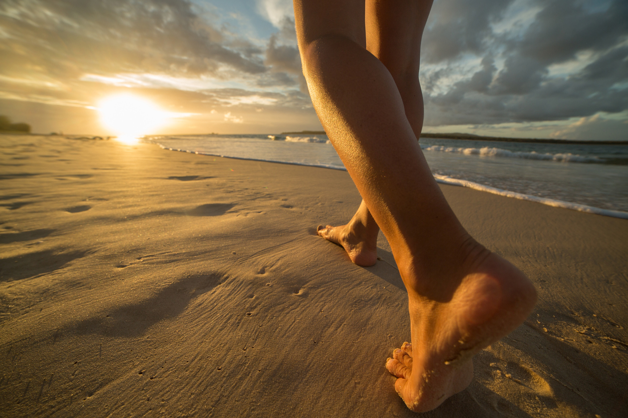Young woman walking on a beach making foot print on the sand. Sun setting on the sea.