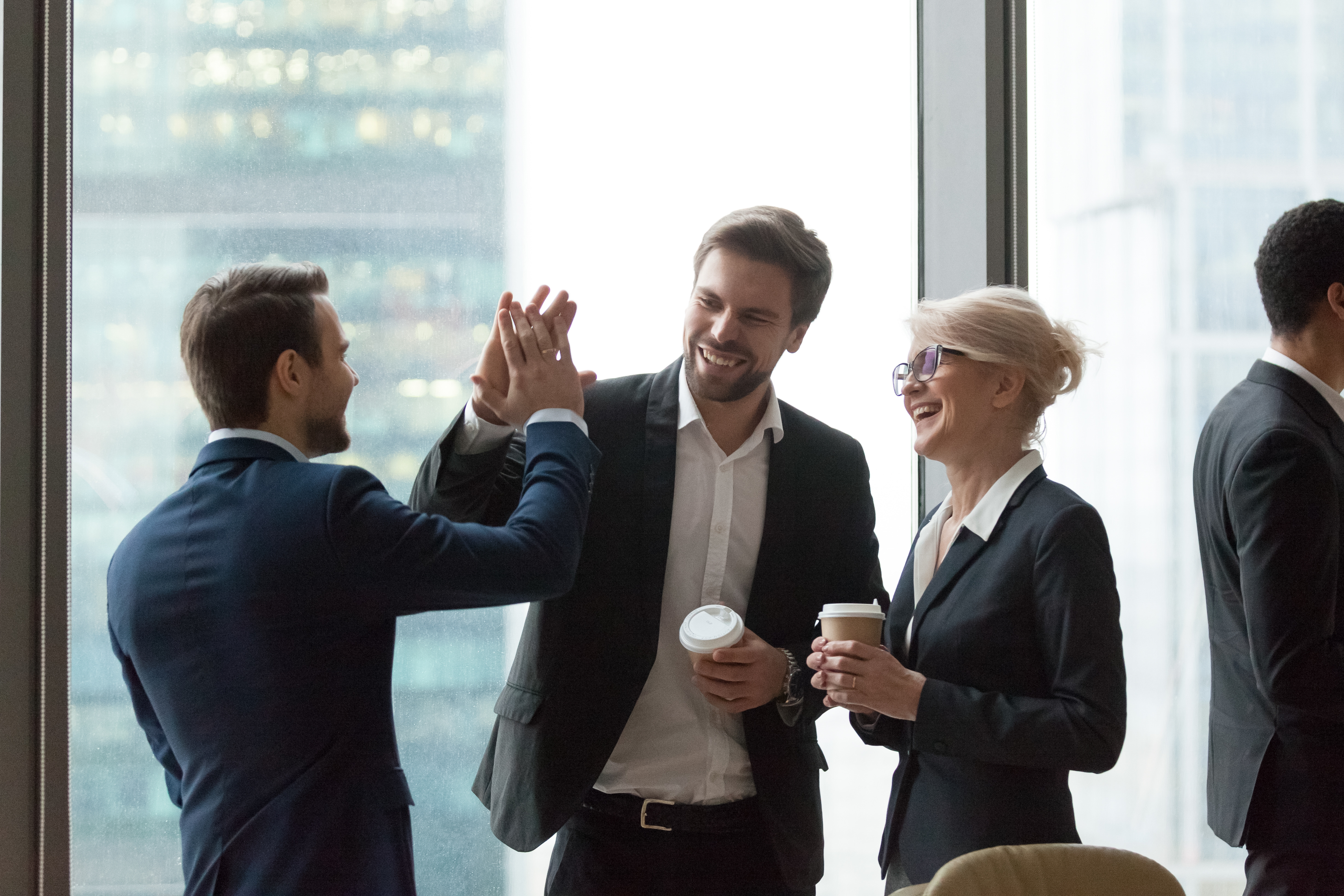 Happy executives have fun give high five during friendly talk in office, cheerful employees laugh celebrate funny joke, share success and good teamwork result motivated by great corporate relations