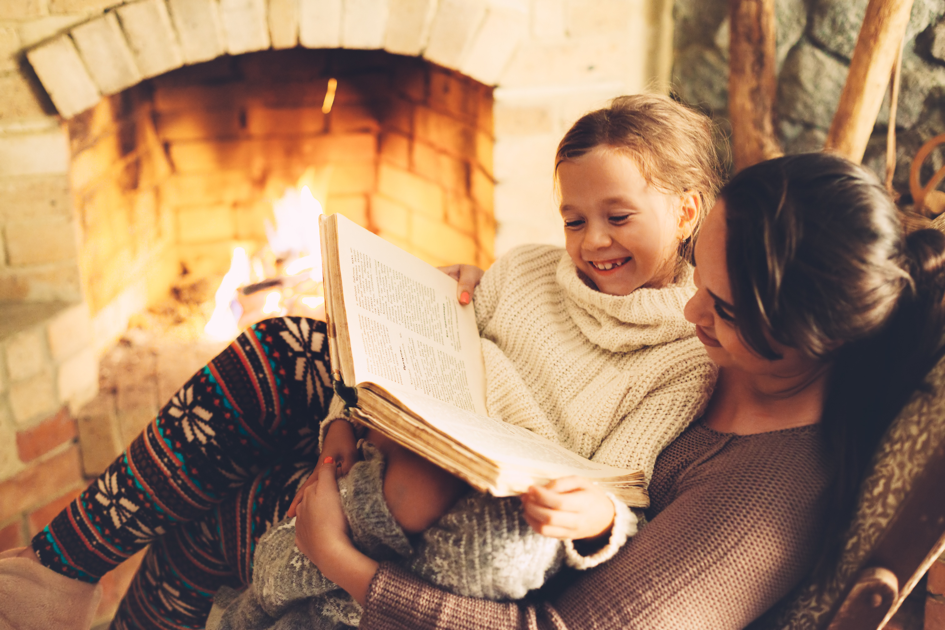 Mom with child reading book and relaxing by the fire place some cold evening, winter weekends, cozy scene