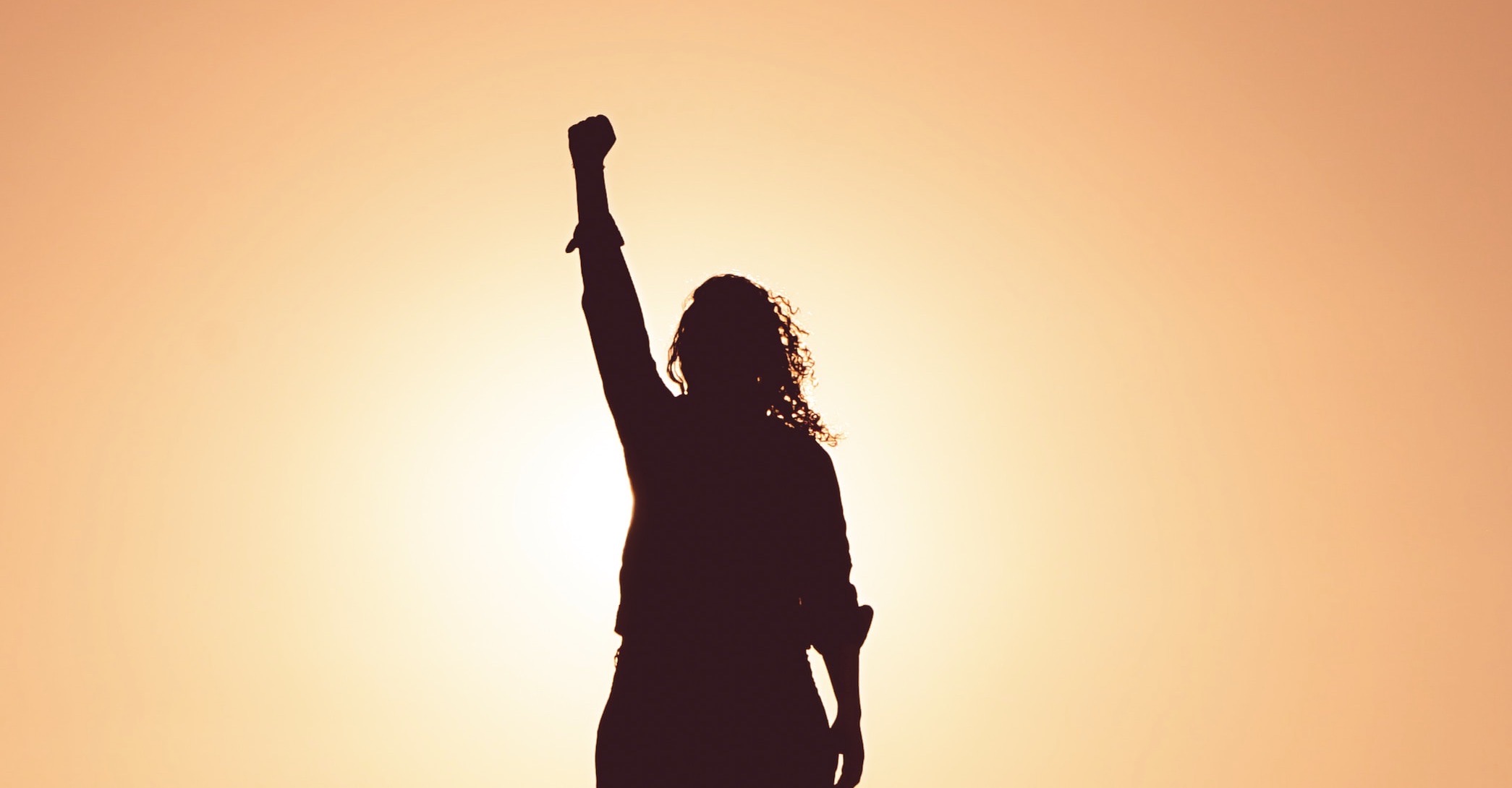 Woman with arm up in victory in front of a sunset