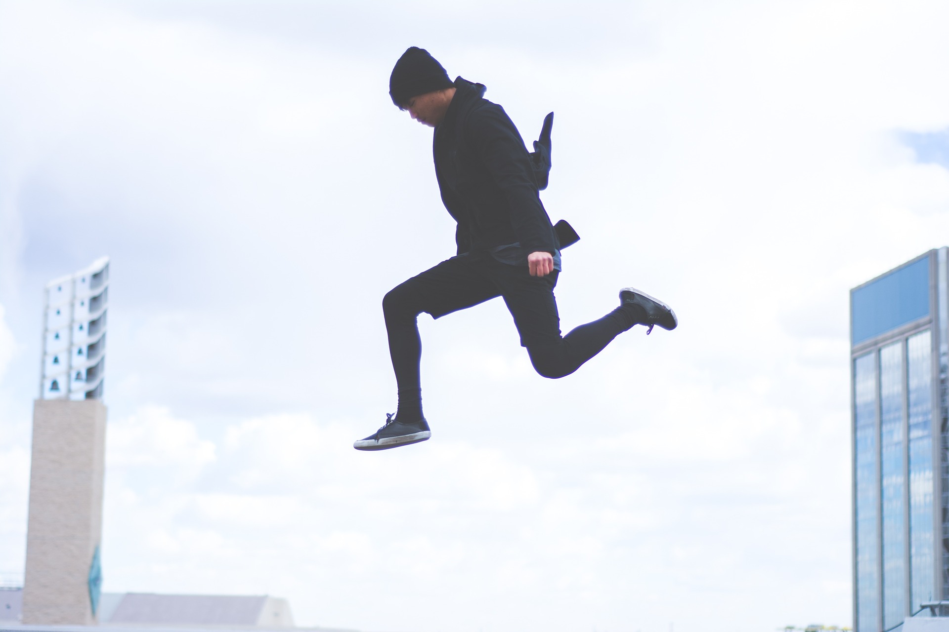Man dressed in black jumping through the air with buildings in the background.