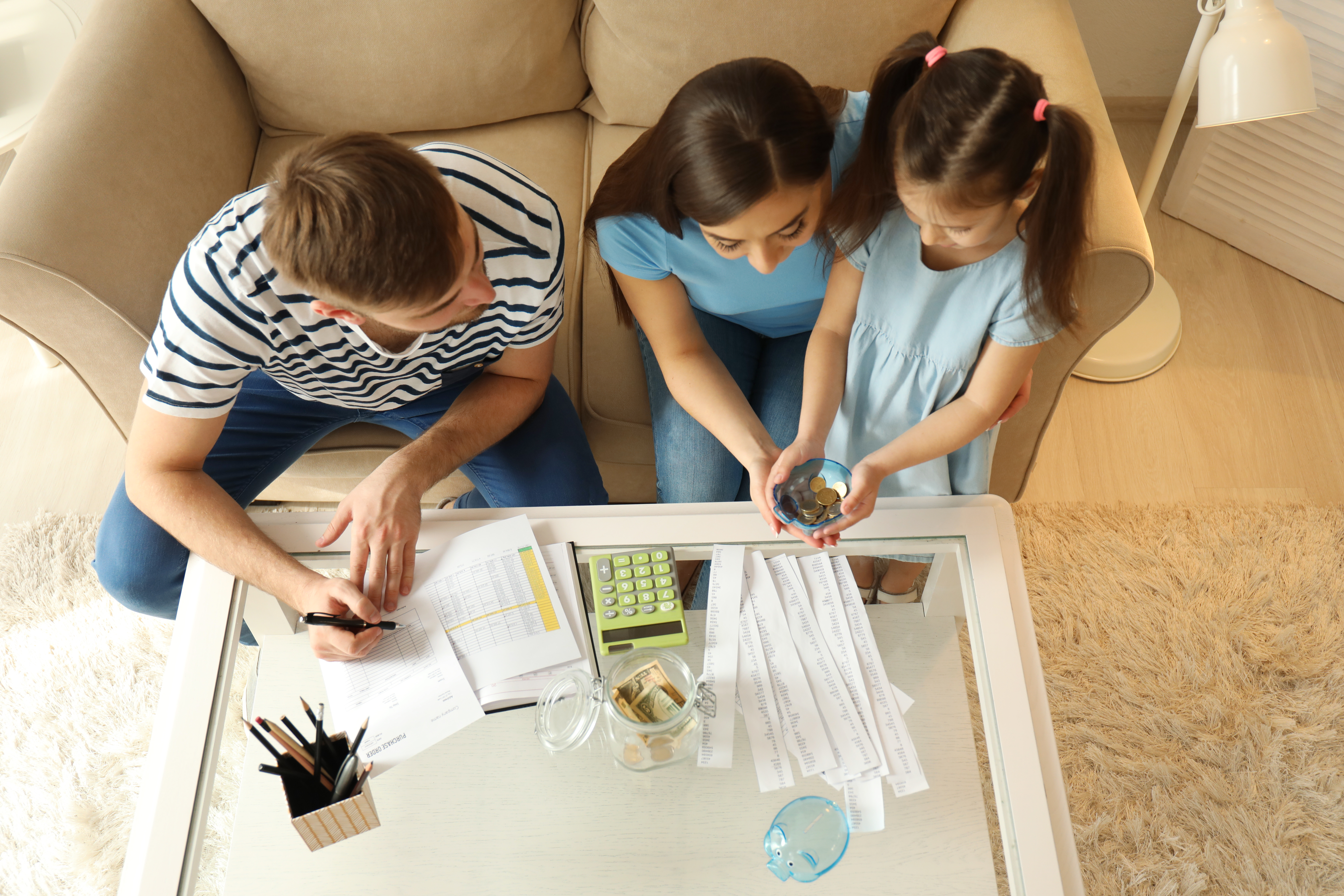 Family paying bills together, using a calculator and counting money in living room.