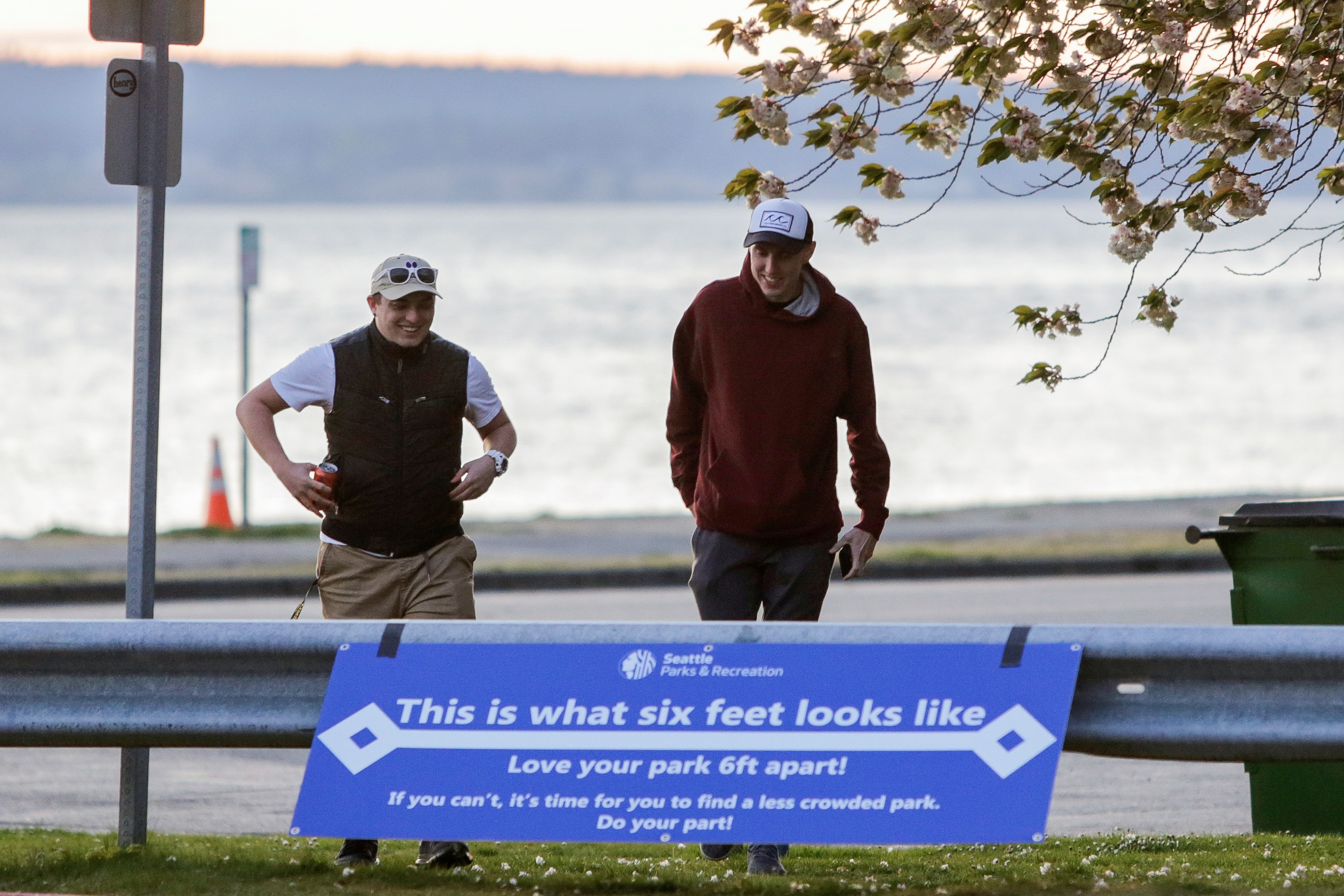 People walk past a sign at Golden Gardens Park asking people to stay six-feet apart after Seattle Mayor Jenny Durkan reopened parks that were closed Easter weekend as efforts continue to help slow the spread of the coronavirus disease (COVID-19) in Seattle, Washington, U.S. April 19, 2020.  REUTERS/Jason Redmond
