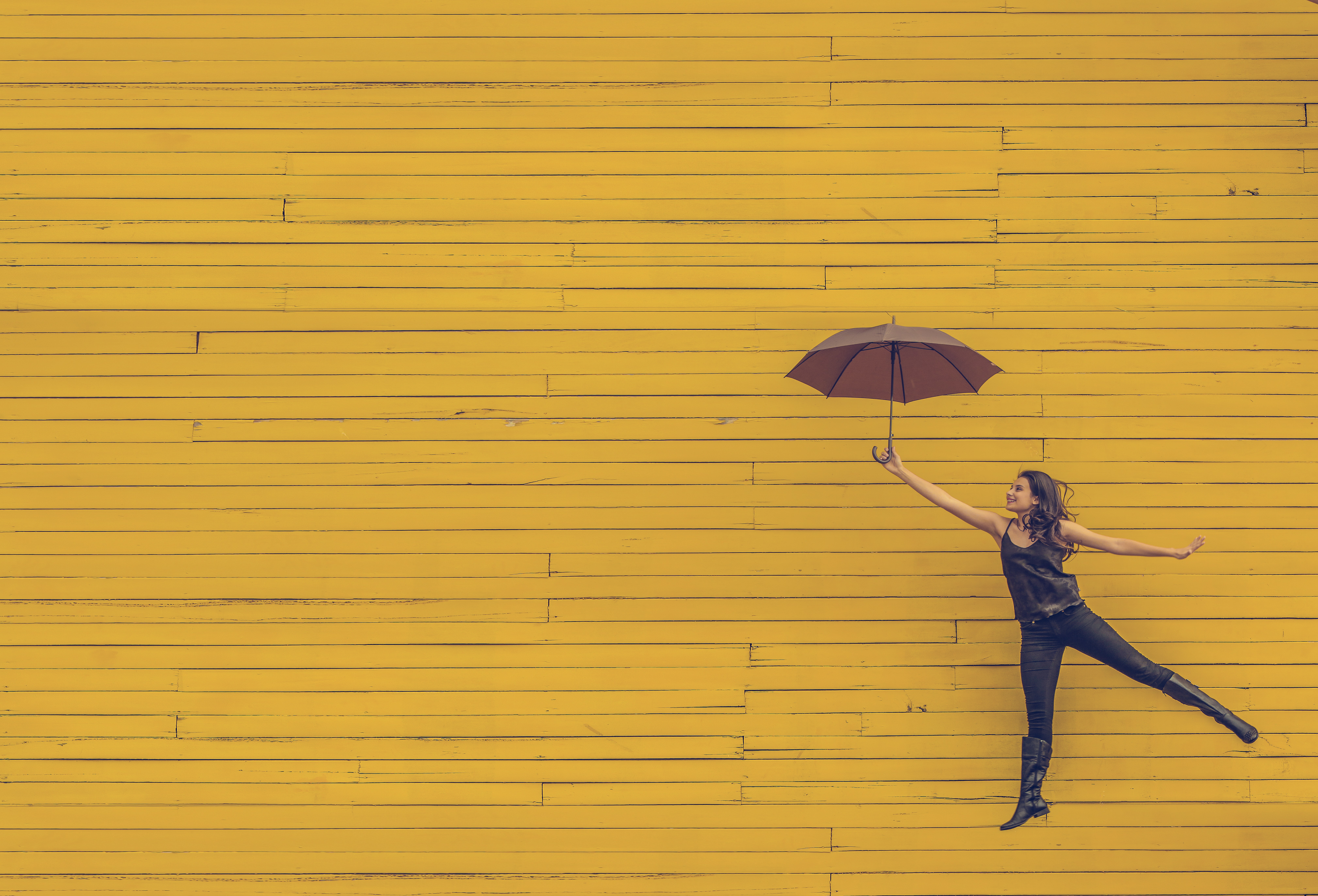 Girl holding an umbrella in front of yellow wall