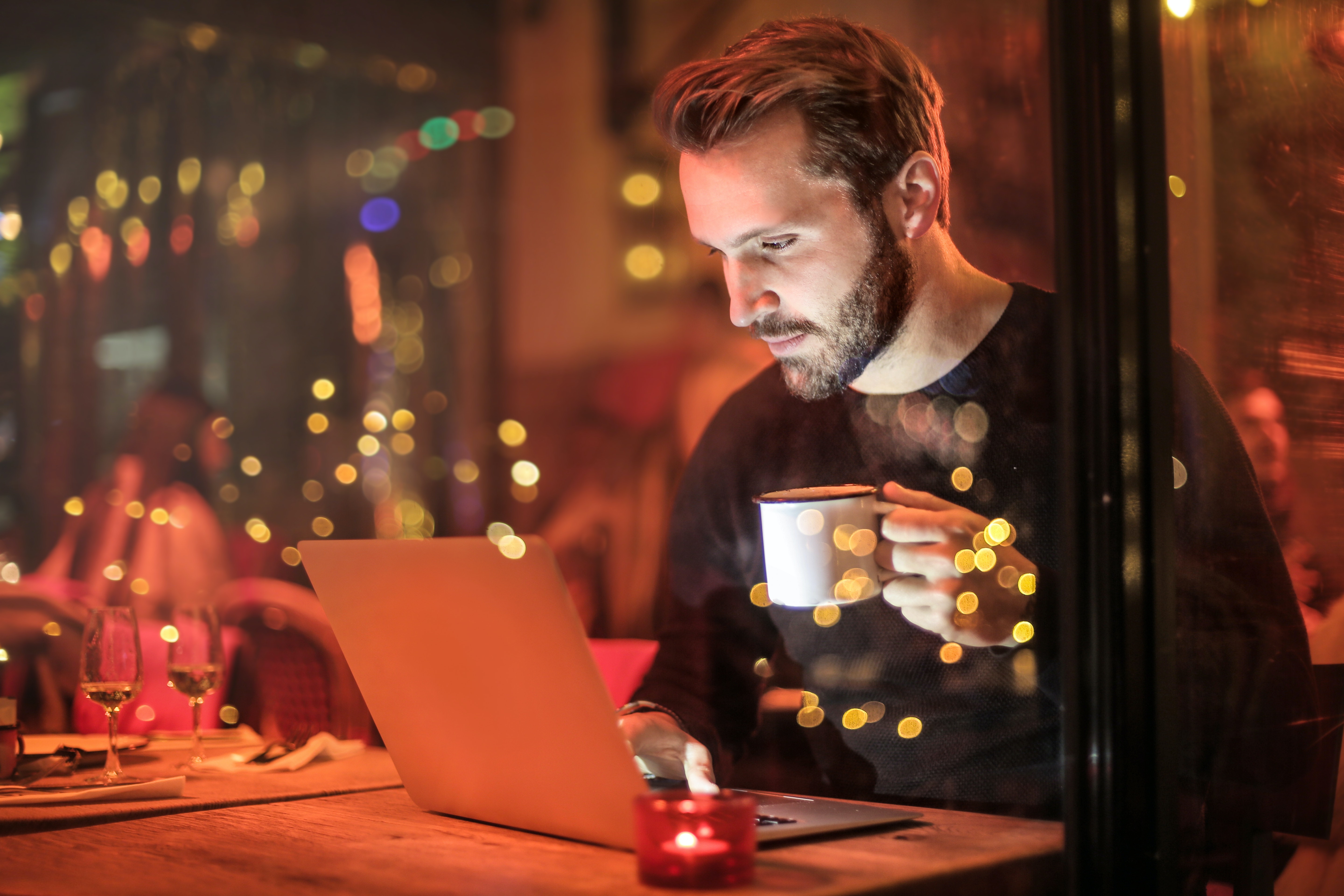 Man in a black sweater holding a cup of coffee and staring down at his computer.