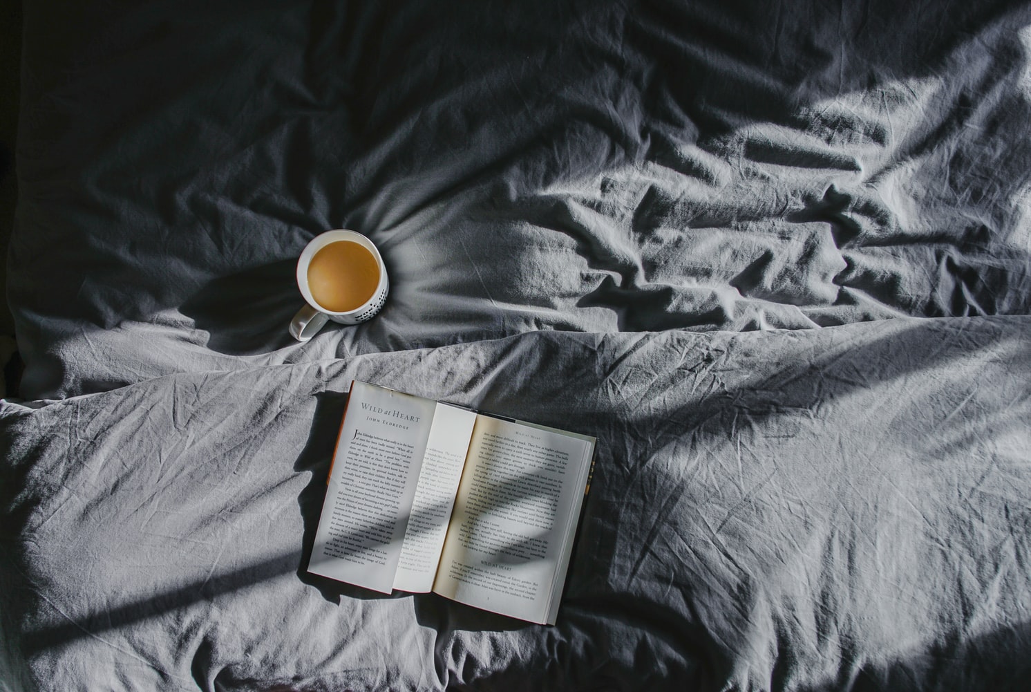 Coffee and a book on a gray bedding