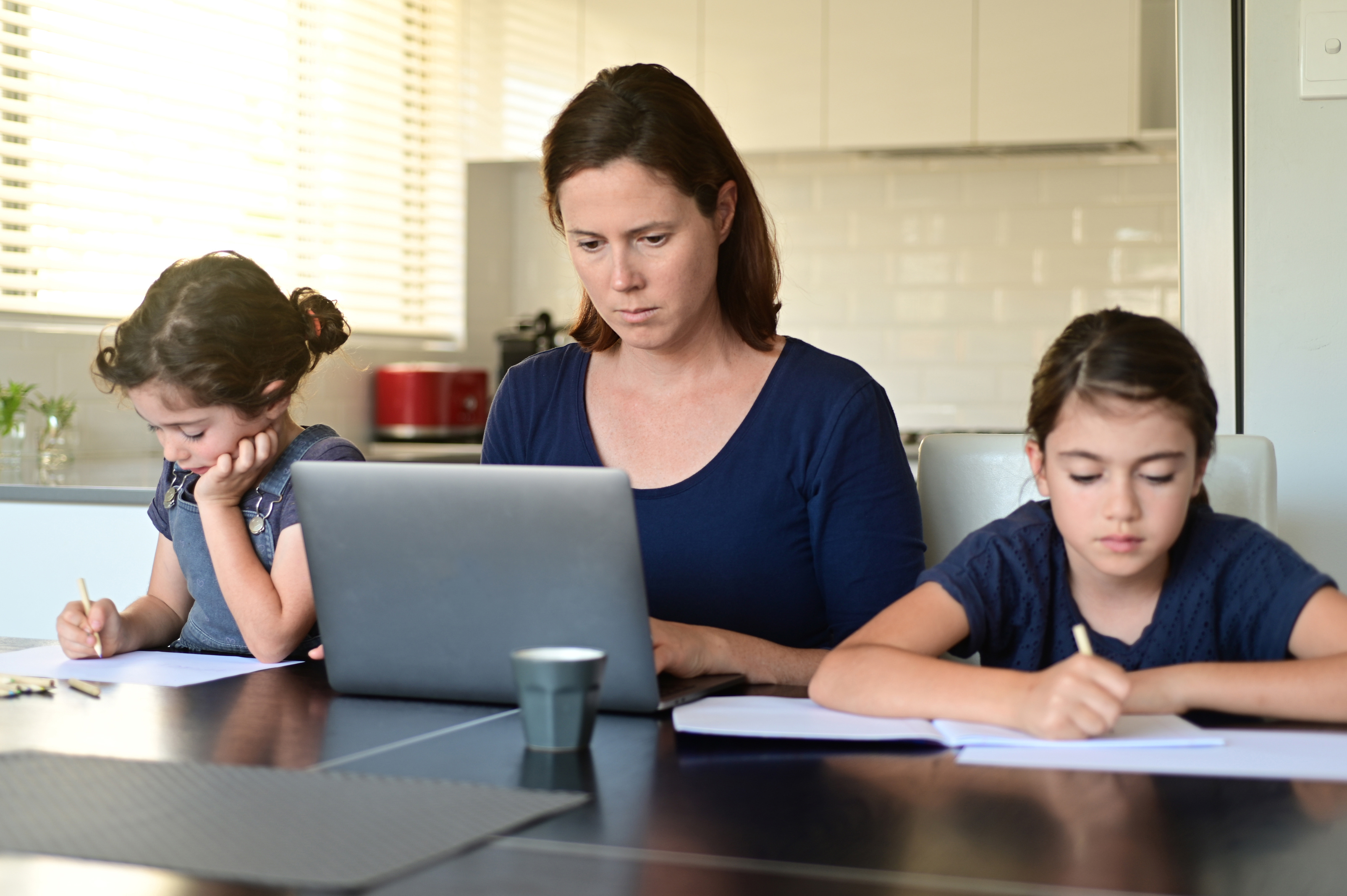 Mom working from home with daughters doing schoolwork.