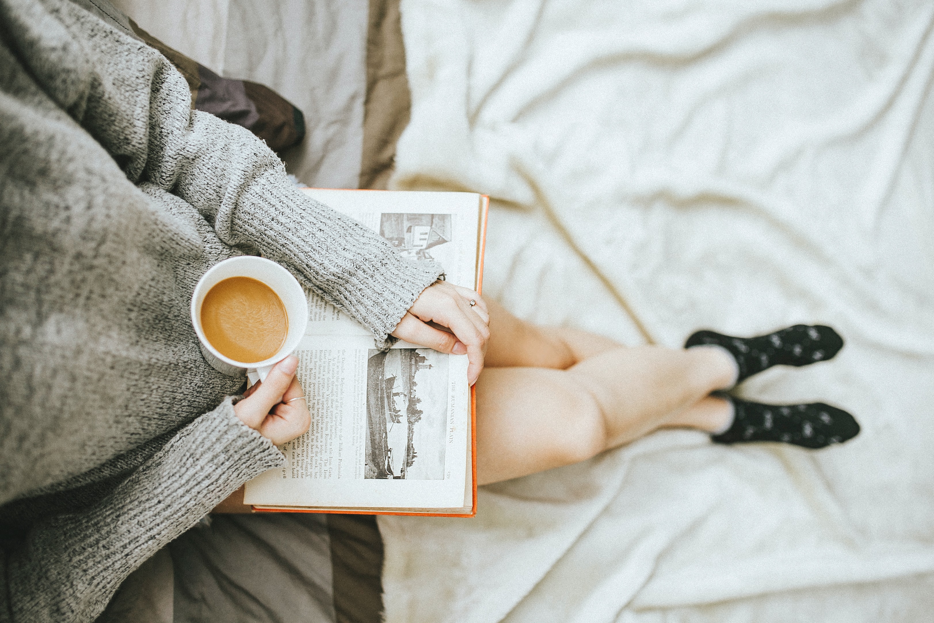Woman sitting on bed with coffee and book