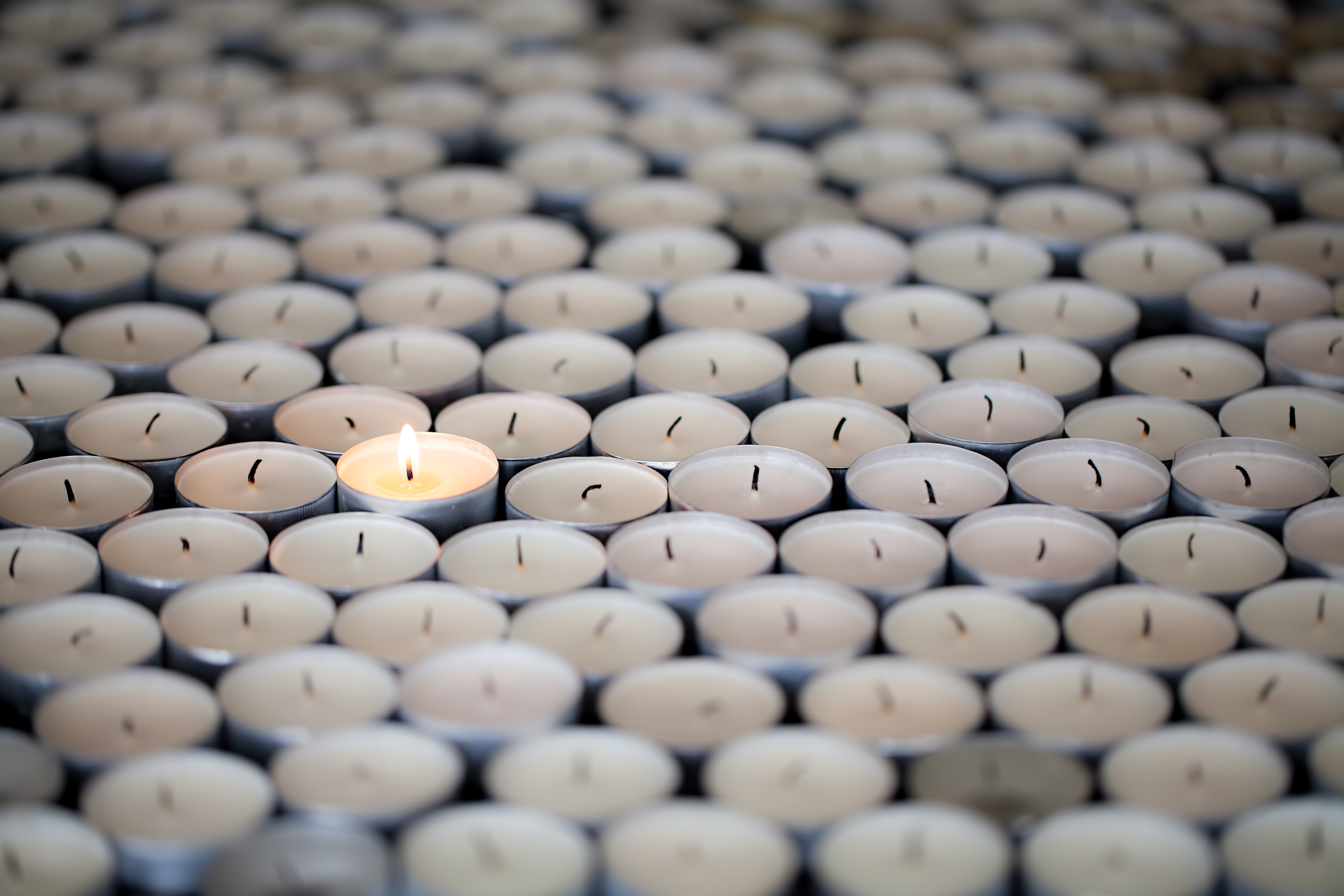 Standing alone. Single resilient flame keeps burning amongst many extinguished tealight candles. Solitary shining light stands out with selective focus.