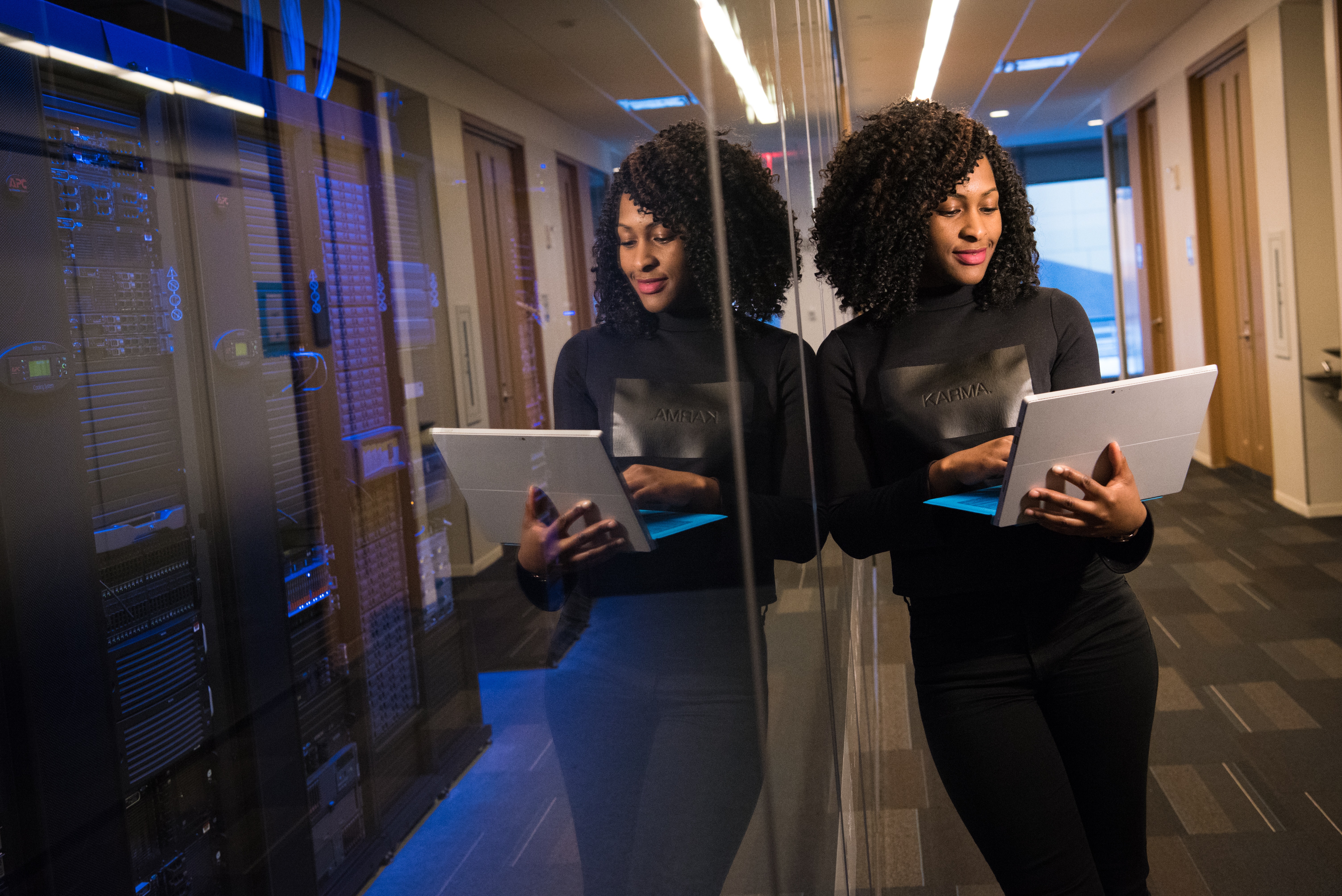 African-American woman holding laptop and leaning against glass wall in office
