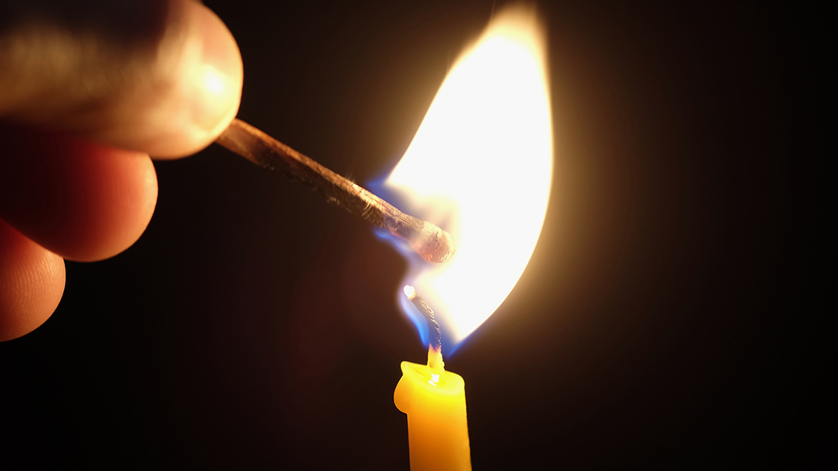hand ignite a yellow candle with match stick on black background
