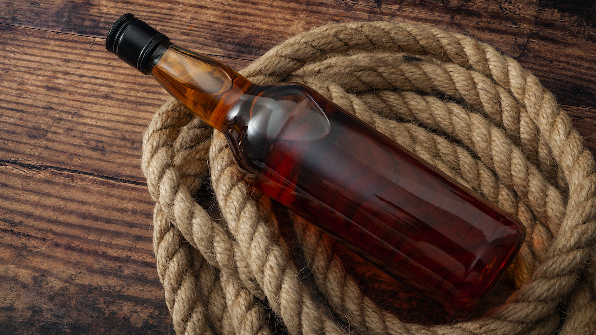 alcoholism in rural america and excessive distilled alcohol and hard liquor drinking concept theme with a bottle of scotch whiskey or brandy and rope lasso on the wooden floor in rustic dark barn
