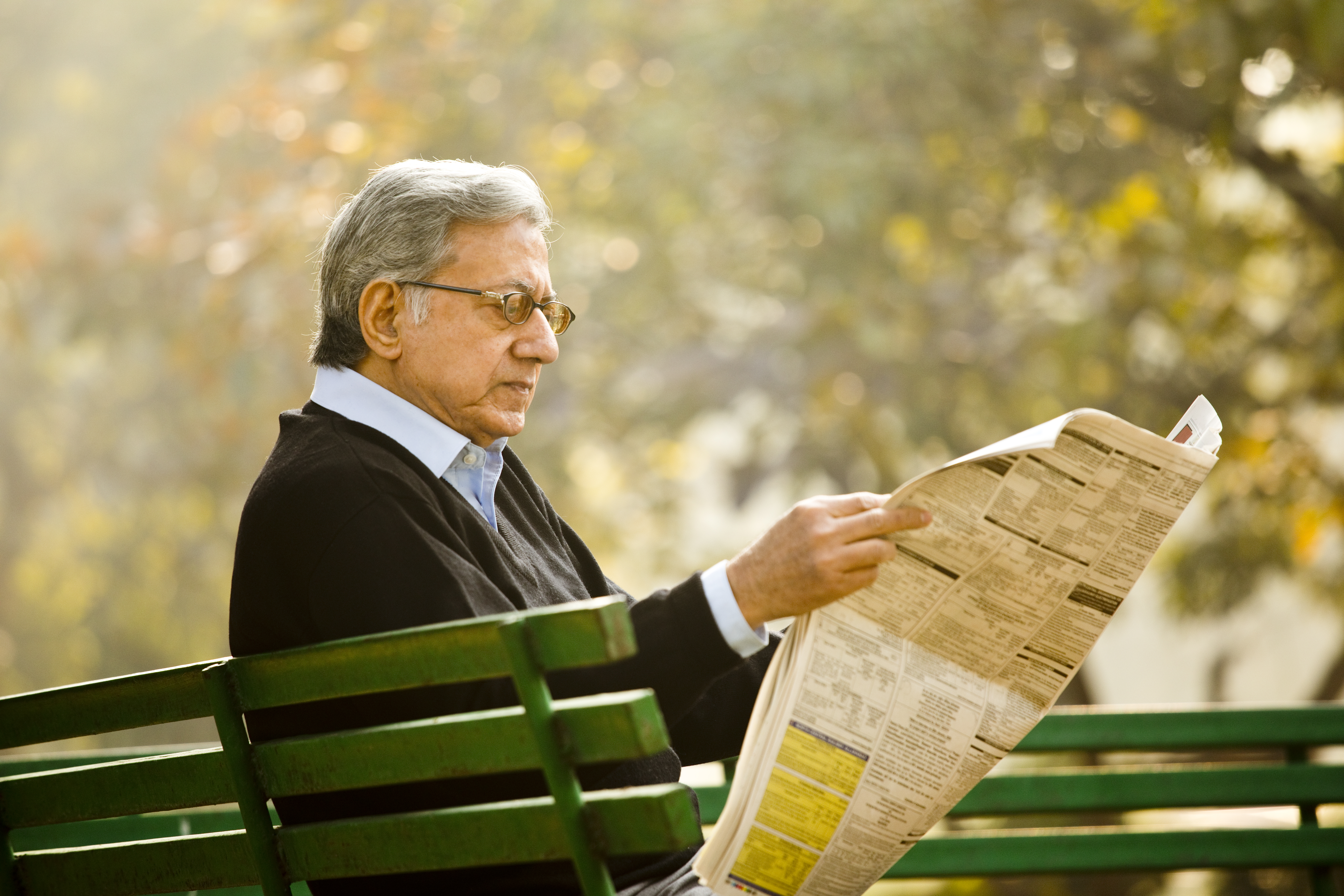 Older man sitting on bench and reading a newspaper in the park