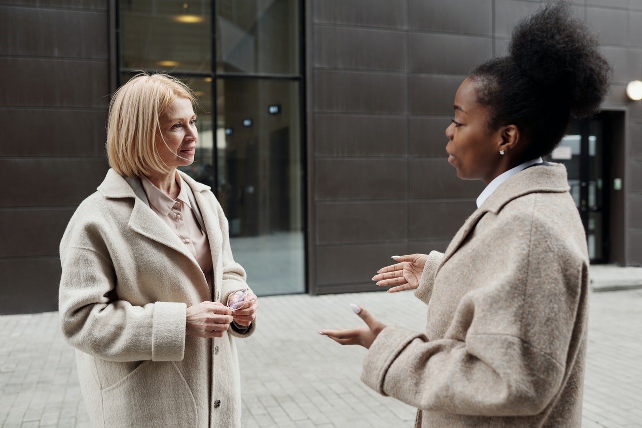 A caucasian women speaking with a black American woman both in business attire