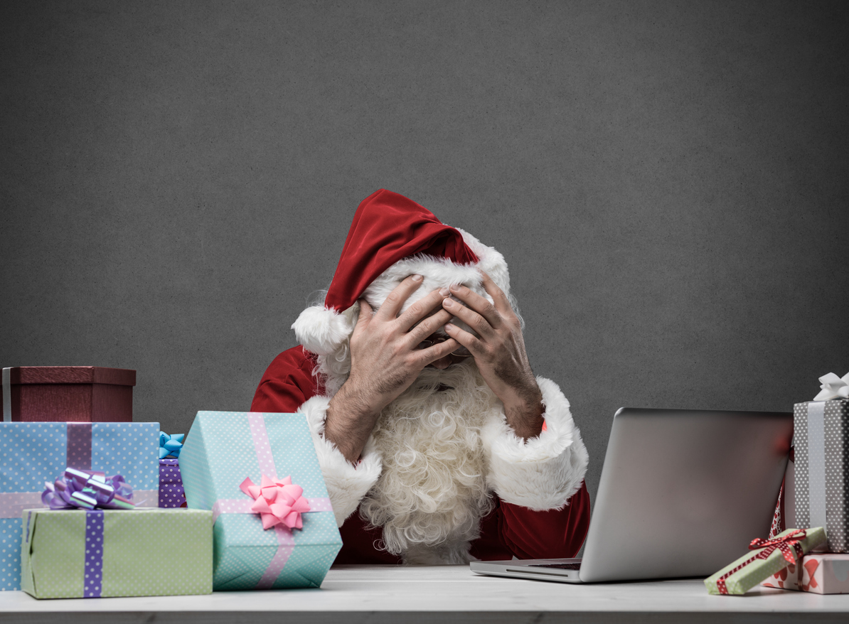 Stressed frustrated Santa Claus with head in hands  connecting with his laptop, he is having computer problems on Christmas Eve