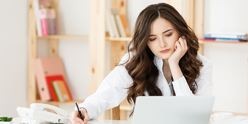 Young attractive woman at a modern office desk, working with laptop and thinking about something.