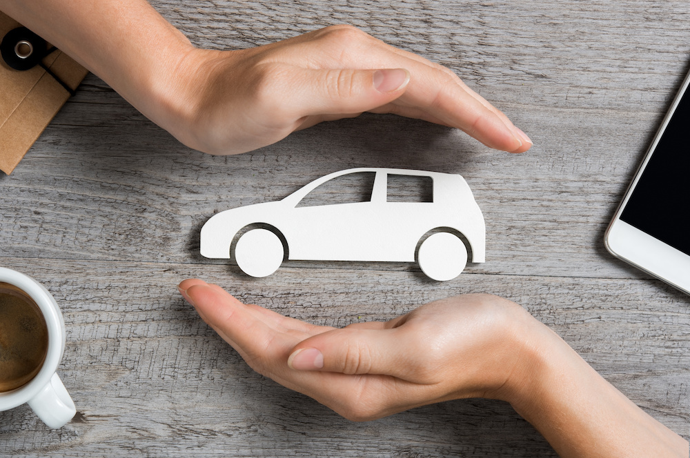 Hands protecting icon of car over wooden table. Top view of hands showing gesture of protecting car. Car insurance and automotive business concept.