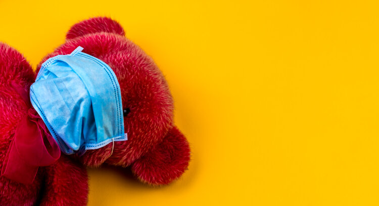 Lonely Red Teddy bear in a protective medical mask on a yellow background with respiratory masks. Coronavirus covid-19 prevention concept.