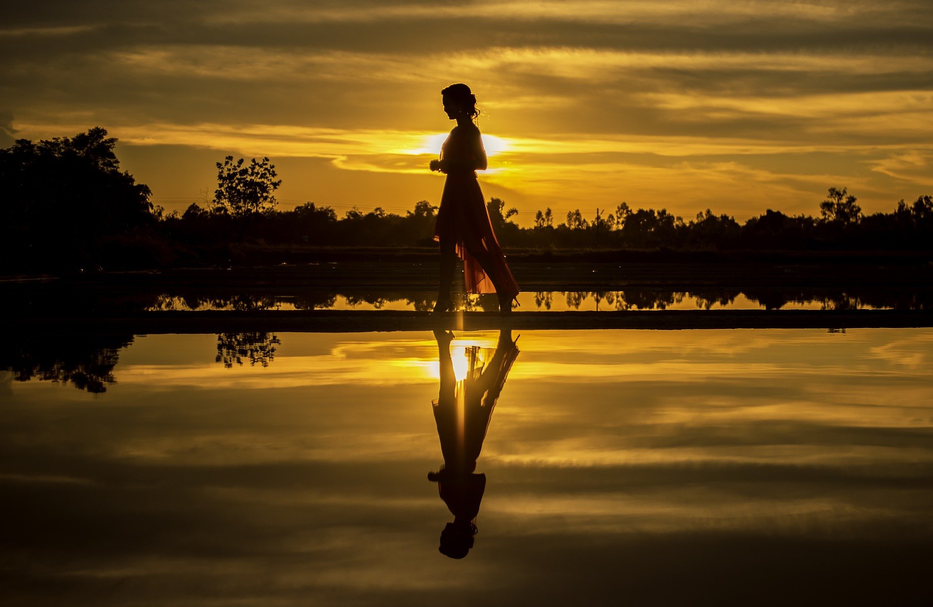 a woman walking with the orange and golden sunset behind her