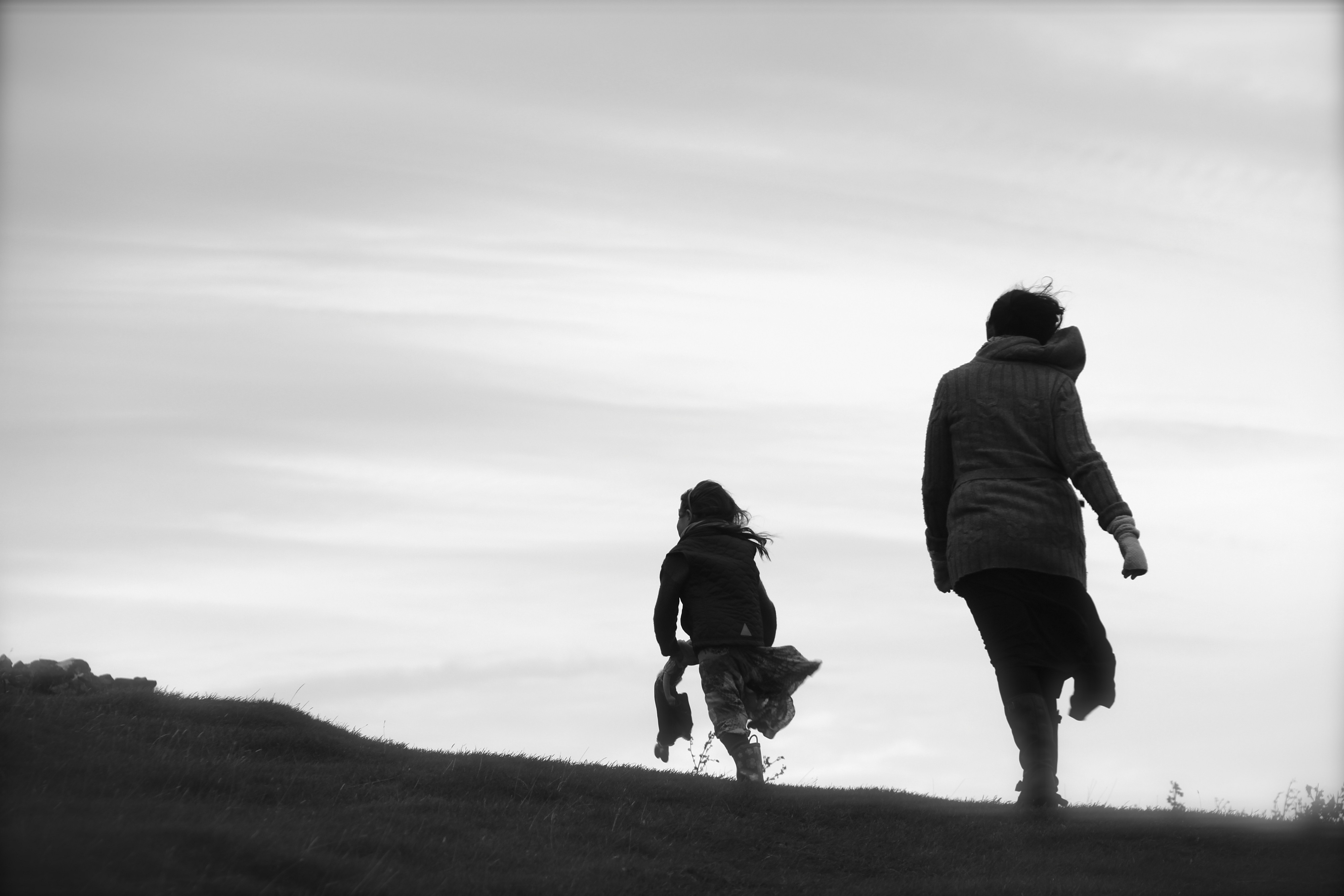 Black and white image of mother and daughter walking up hillside in silhouette.