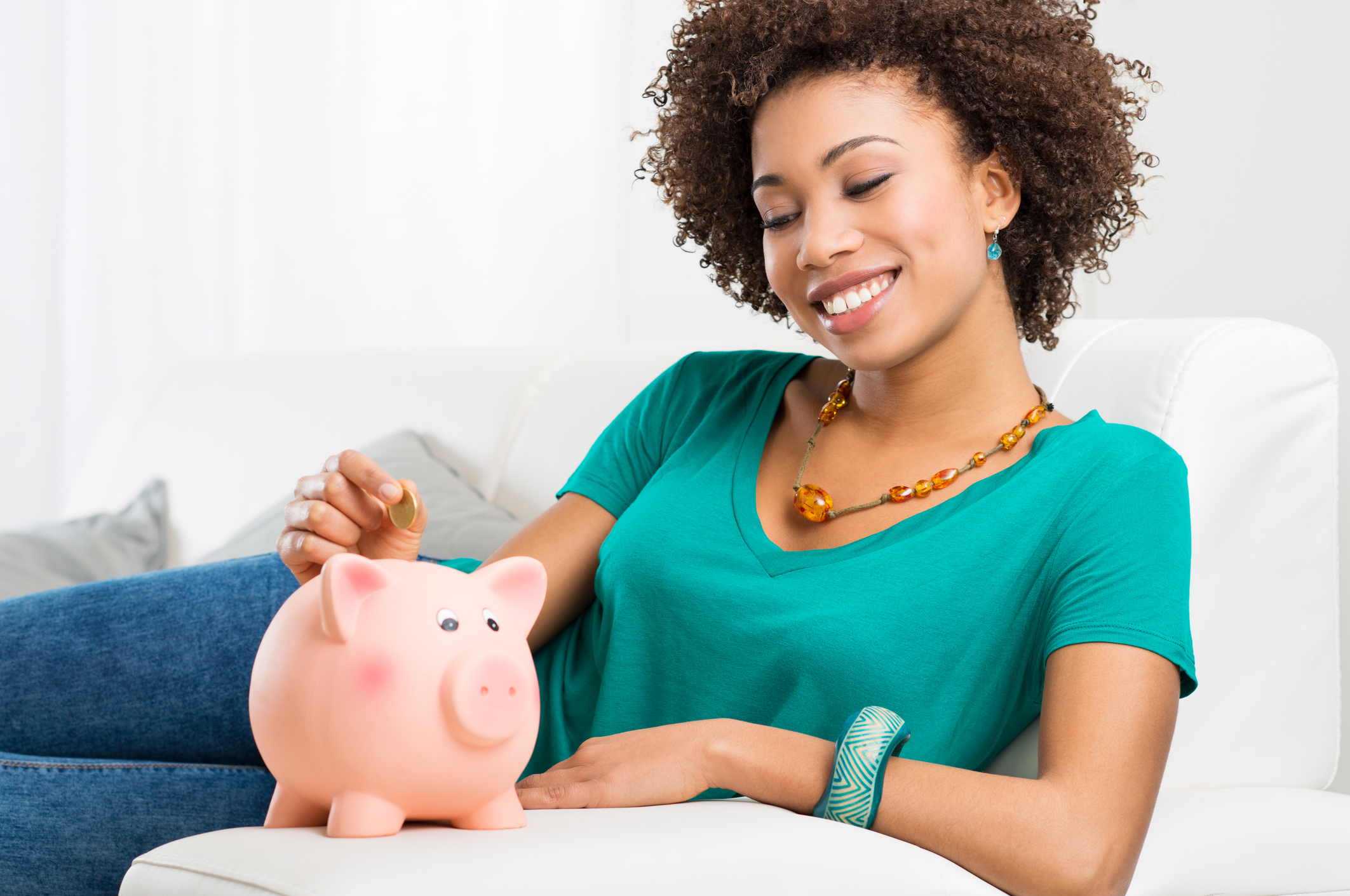 Young Girl Lying On Couch And Putting Coin In Piggybank