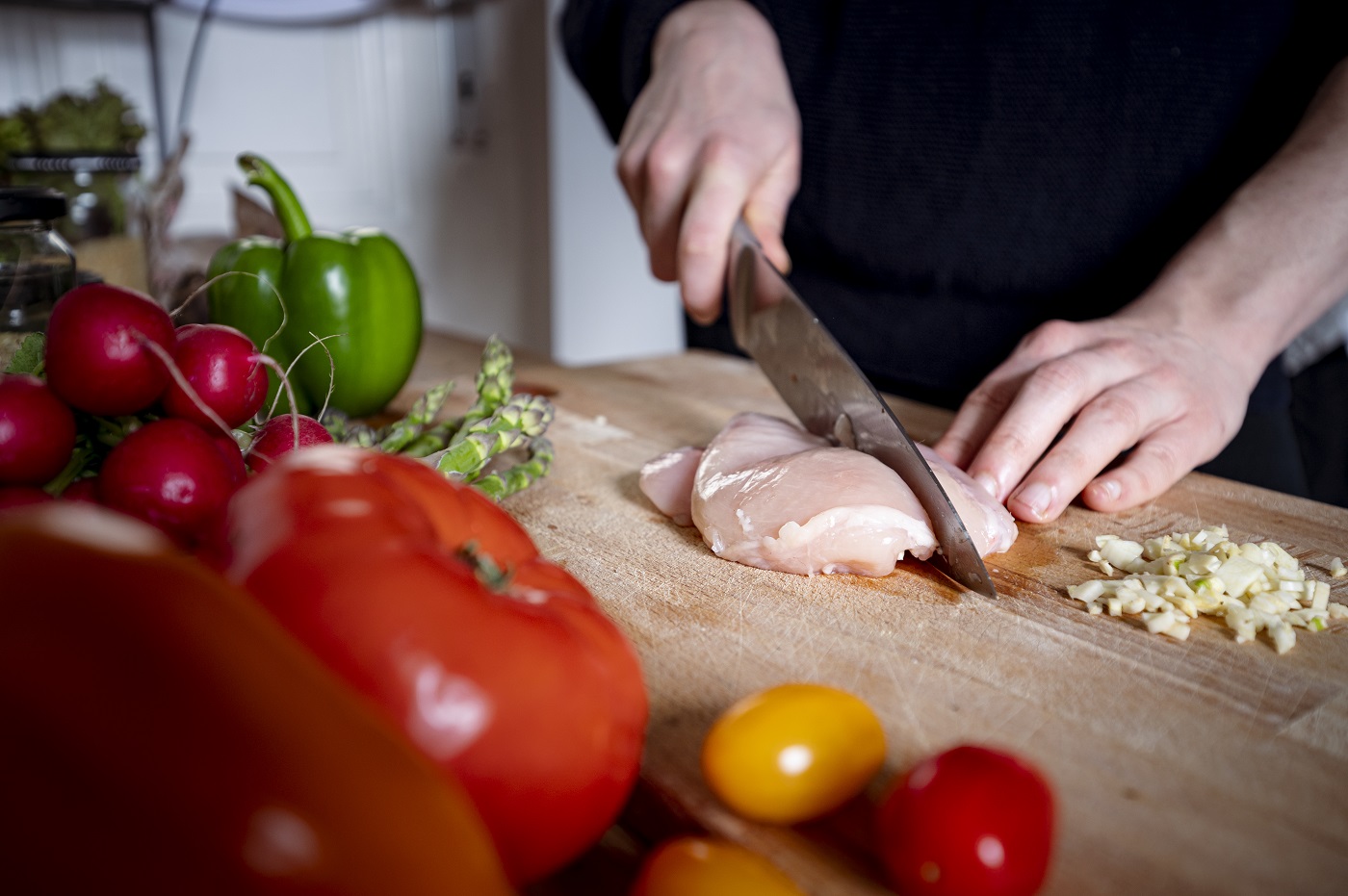 A person cuts a chicken fillet on a cutting board with a kitchen knife.
