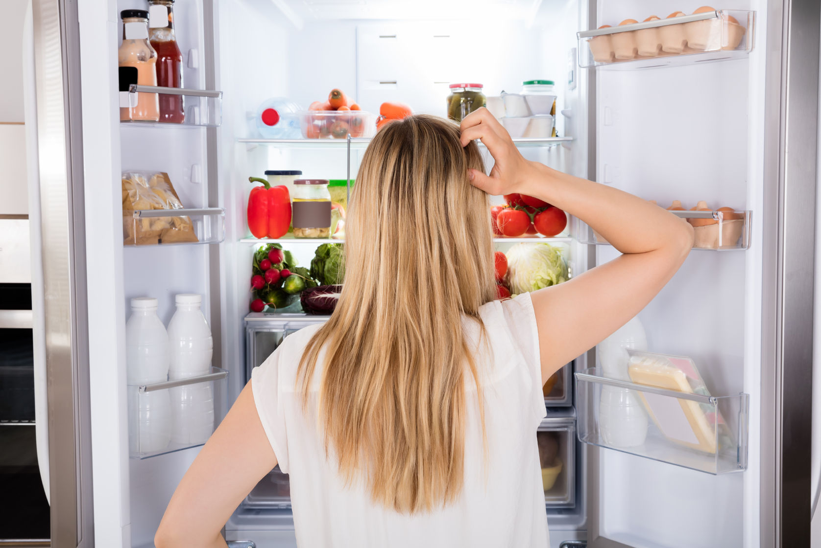 70309104 - rear view of young woman looking in fridge at kitchen