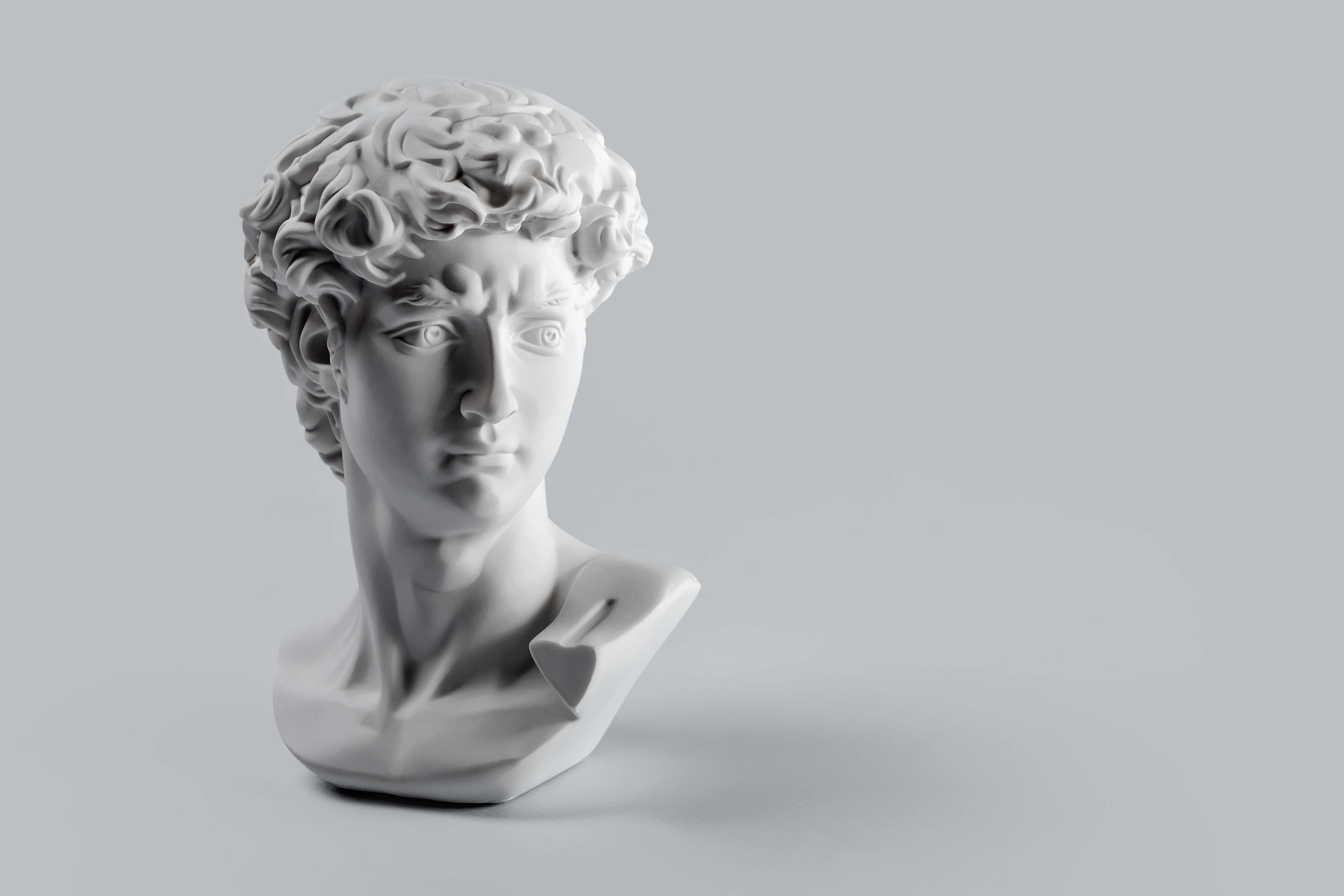 Gypsum statue of David&#039;s head. Michelangelo&#039;s David statue plaster copy on grey background with copyspace for text. Ancient greek sculpture, statue of hero.