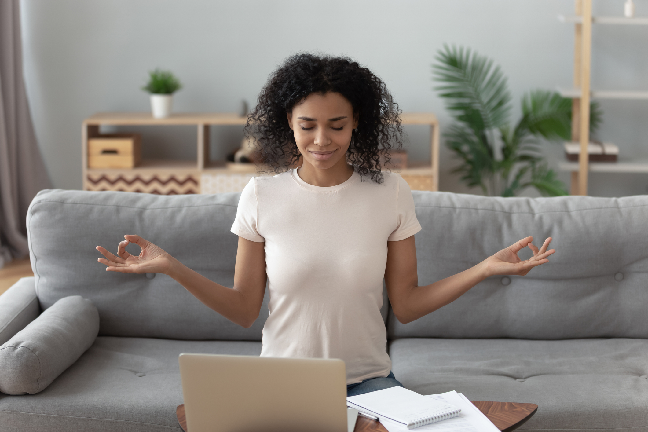 Serene happy calm african girl student sit on couch take break from computer work study do yoga exercise breath fresh air at home, mindful healthy woman relax meditating feel no stress free concept
