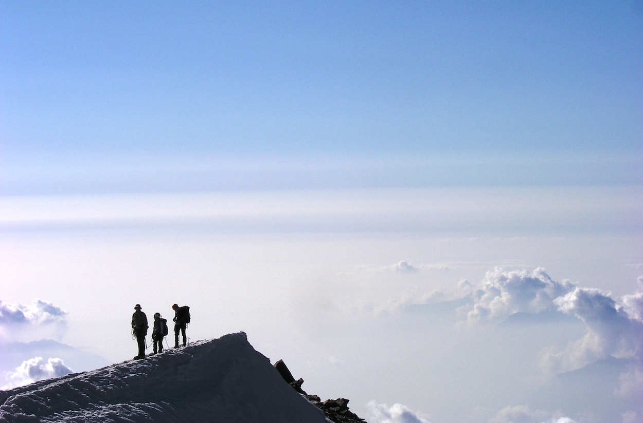 Three climbers on an icy ridge over the clouds