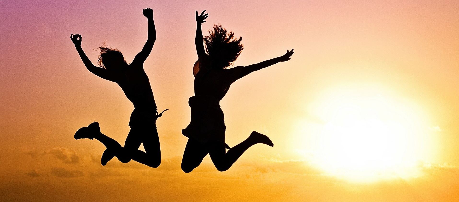 Two people jumping for joy against a sunrise