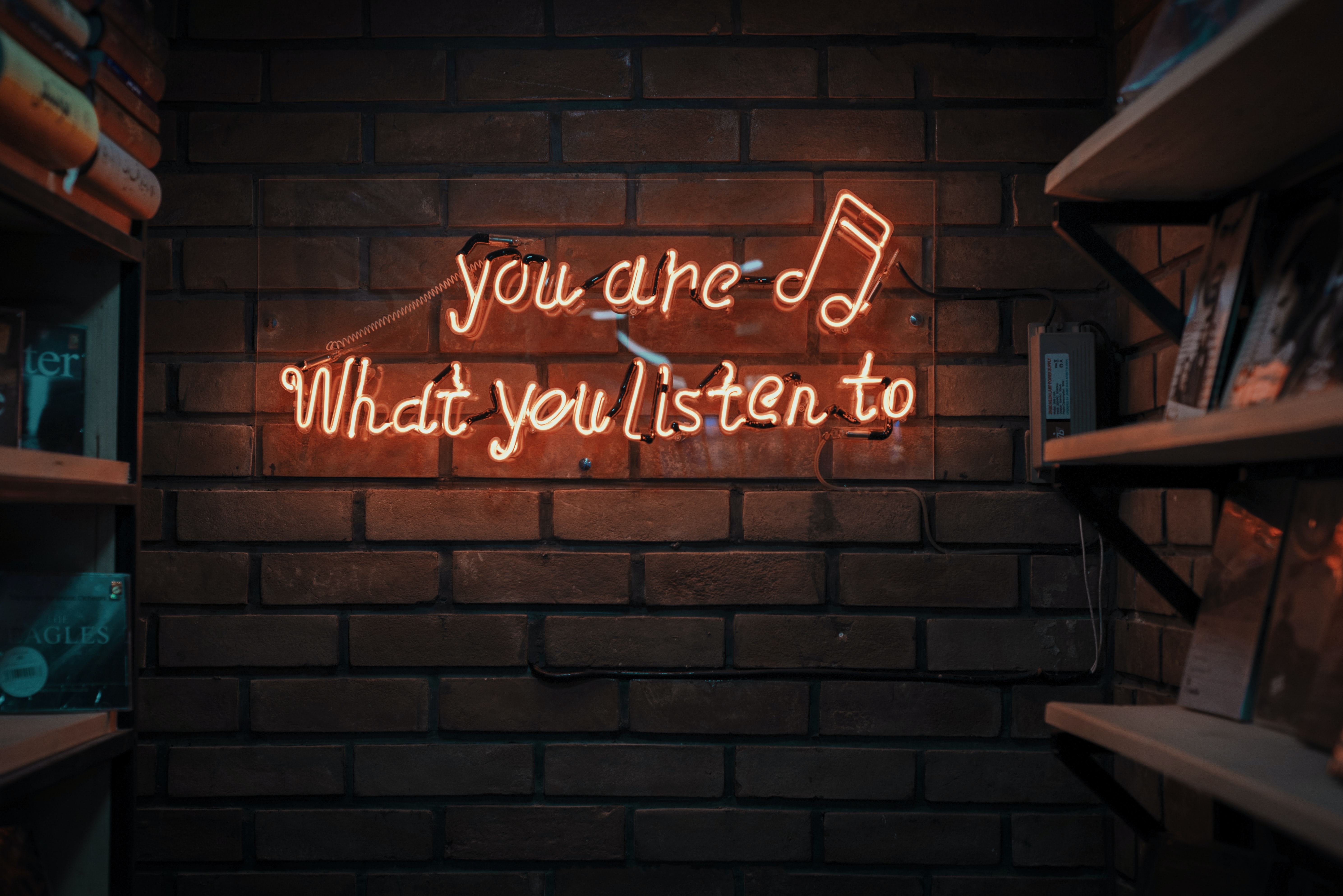 Photo of you are what you listen to text spelled in lights by music notes on brick wall. Photo on Dr. James Goydos 2021 article on physician health podcasts