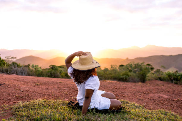 Young woman sitting on the ground, enjoying nature, with the sunset in the background.