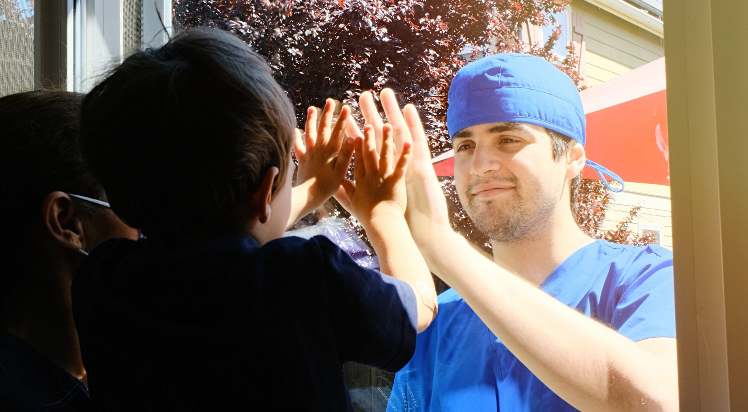 Young Healthcare worker posing seeing his son with a window glass separating them to avoid possible contagion