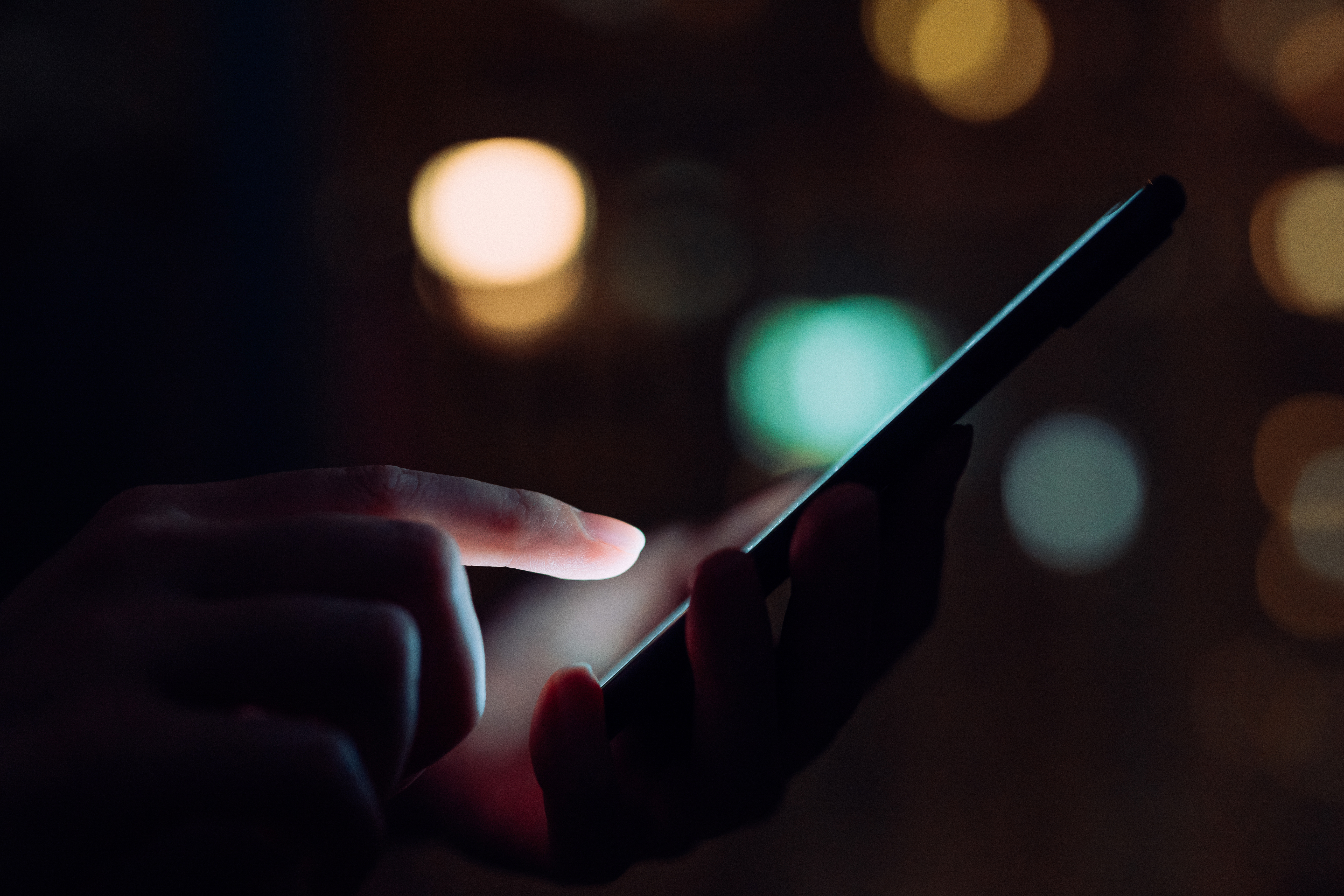 Close up of woman&#039;s hand using smartphone in the dark, against illuminated city light.