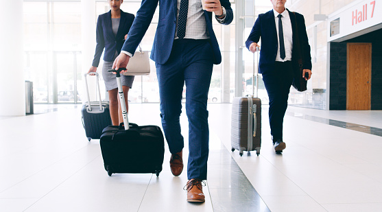 Cropped shot of three unrecognizable businesspeople walking and pulling suitcases while in the office during the day